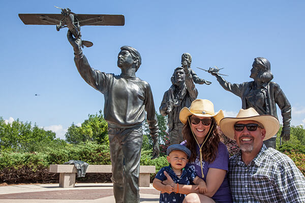 Family of 3 standing in front of statue with a plane